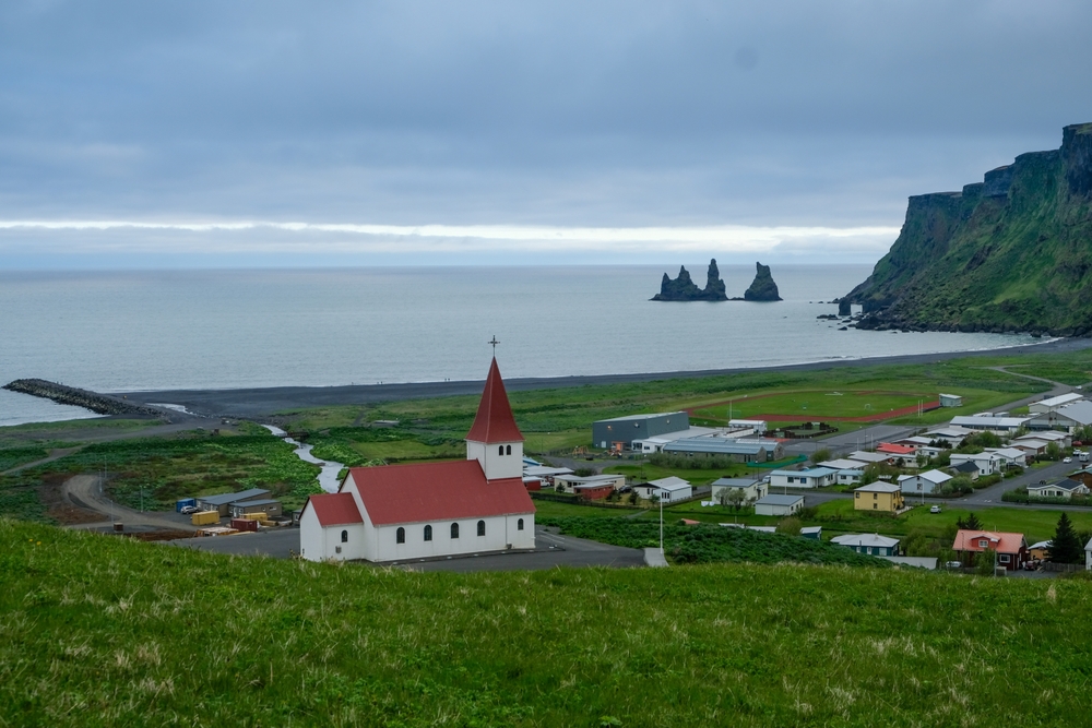 Vík med kirken, den svarte stranden og klippene Reynisdrangar på sørkysten av Island