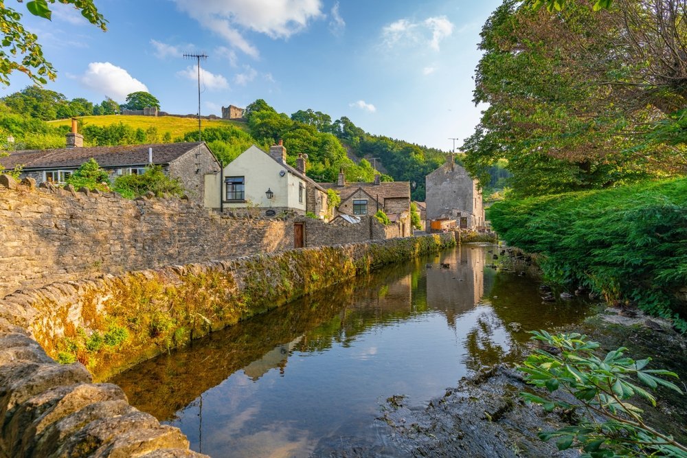 Landsbyen Castleton og bekken med ruinen av Peveril Castle over husene